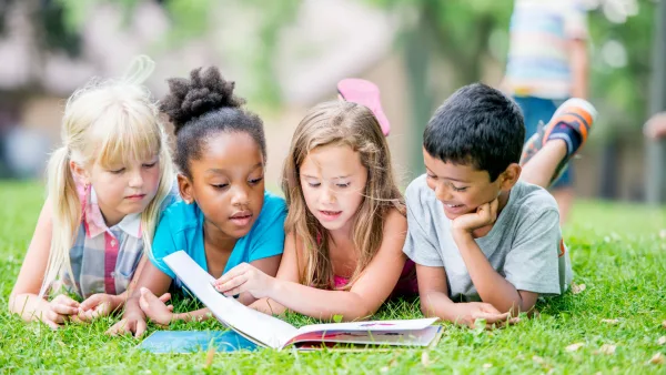 Four children laying on the grass and reading a book together